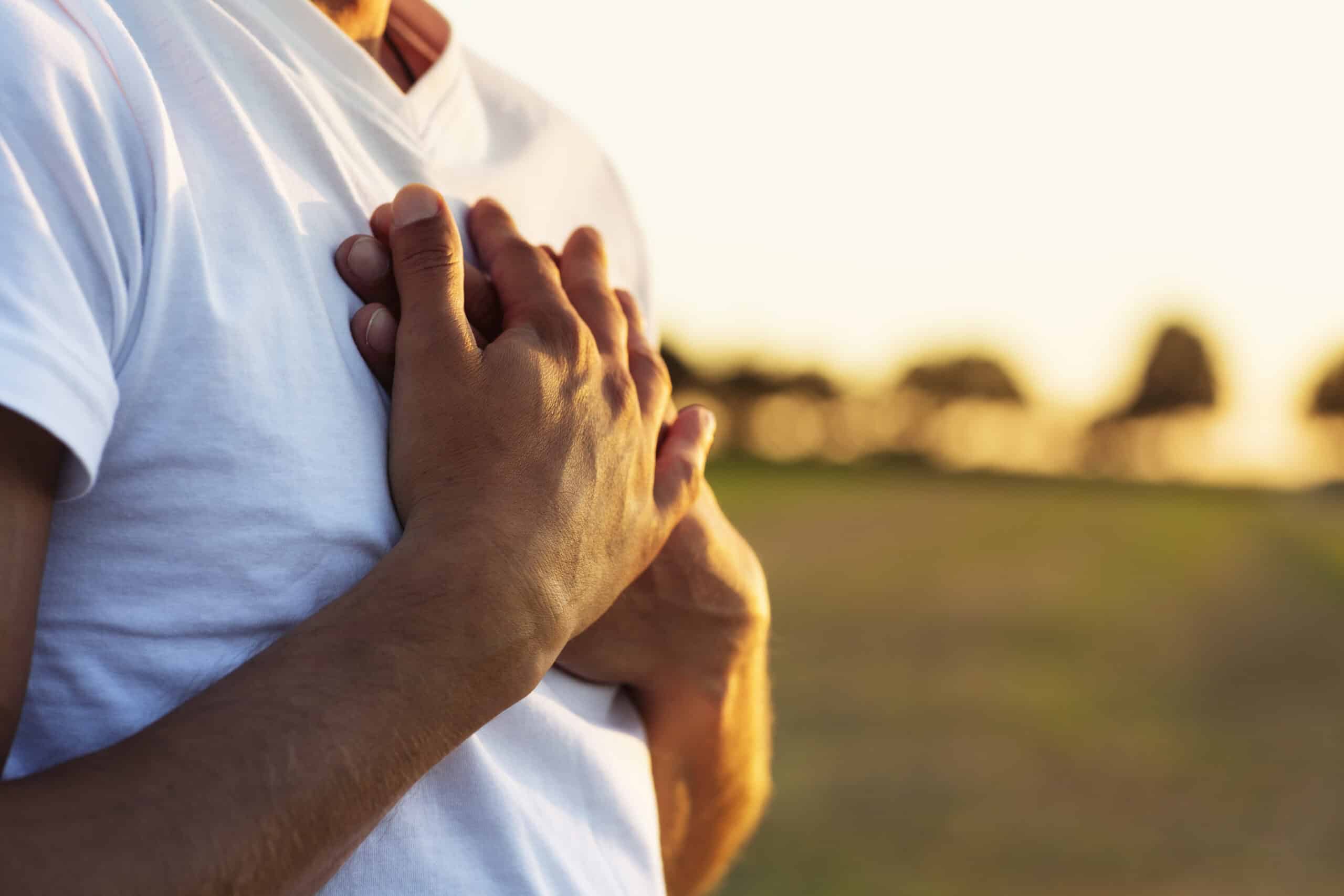 Mann mit beiden Händen selbstmitfühlend auf dem Herzen im Sonnenaufgang